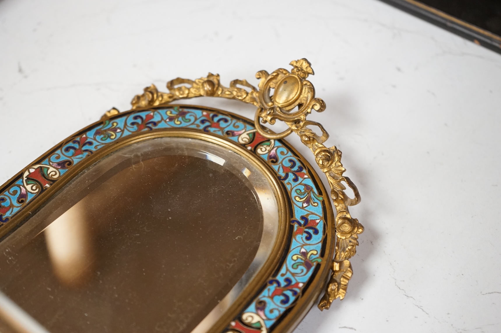 A champleve enamel easel mirror with putti supports, 28cm high.